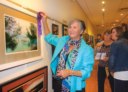 Gail Gallagher of South Jamesport pins the ‘Best of Show’ ribbon on a photo she took three years ago on a trip to Vietnam during the 51st annual Photography Show at Riverhead Free Library Friday evening. The Friends of the Library show was dedicated to Thelma Booker, who has spearheaded the show since 1999. (Credit: Barbaraellen Koch)