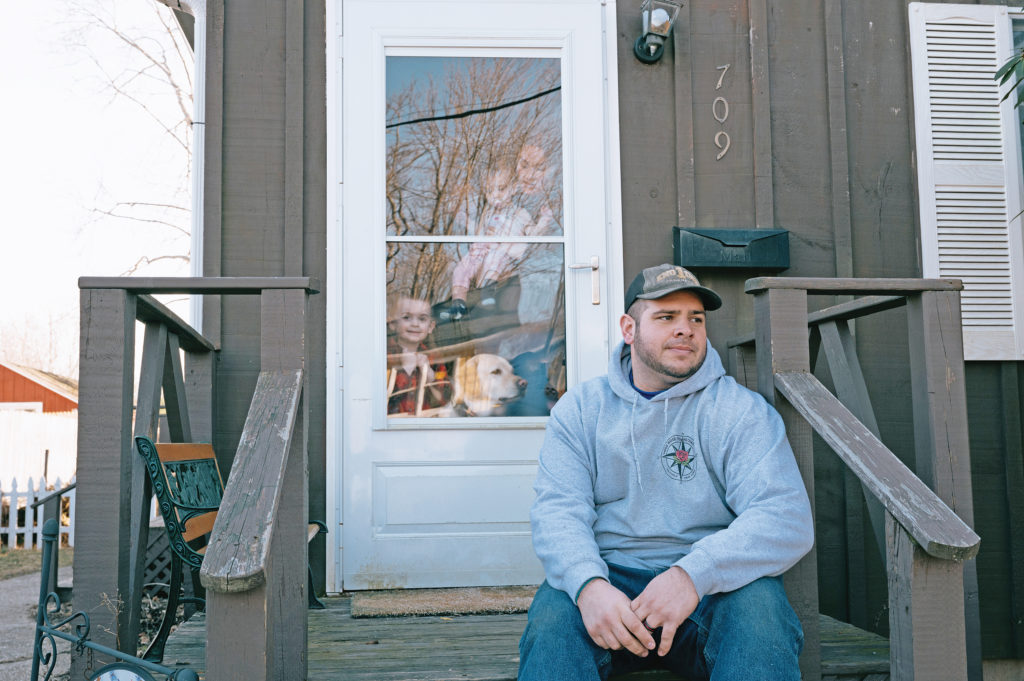 Craig Jobes on the porch of his rental home in Greenport, with his family behind him. The Southold Town employee said he’s considered leaving the North Fork to escape rising prices. (Credit: David Benthal)