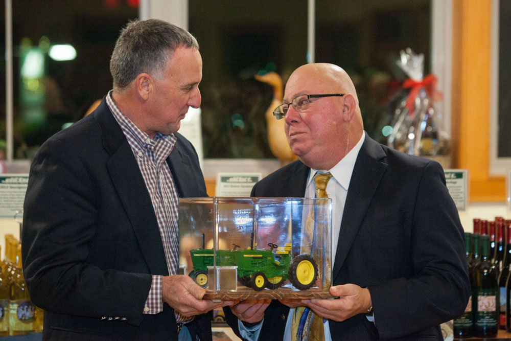 Former Farm Bureau president Mark Zaweski presents Joe Gergela with a miniature tractor as a memento. Also in the presentation case is a small container of soil from Joe's Jamesport farm. (Credit: Katharine Schrieder)