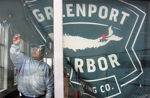 Greenport Harbor Brewing Company worker Enfivfo Cruz cleans windows that line the former Lucas Ford showroom on Main Road in Peconic. The building and an adjoining one are being renovated to house a restaurant and the beer company’s second brewing facility. (Credit: Barbaraellen Koch)