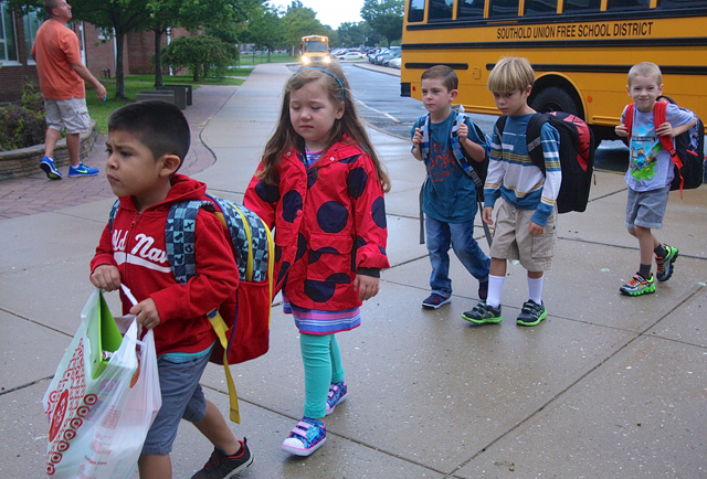 A group of somber kindergartners get off one of the buses first.