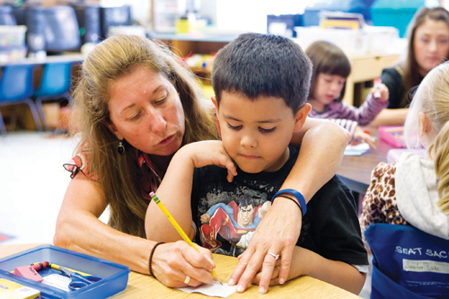 KATHARINE SCHROEDER FILE PHOTO | In a 2010 photo, Oysterponds teacher Jenny Schoenstein helps a kindergartner with a writing exercise. Her name is listed with other teachers expected to be laid off June 30.