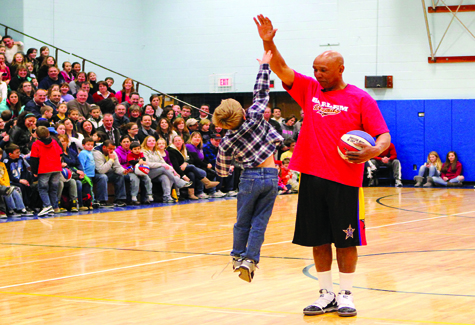 A youngster tries his best to high-five 6-foot, 7-inch Claude Henderson at the Harlem Wizards game at Mattituck High School Thursday night. Proceeds from the sold-out event benefited the Mattituck PTSA.