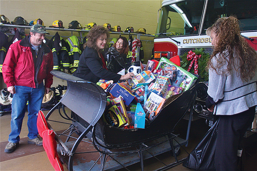 Former Cutchogue Fire Department chief and toy coordinator Tom Shalvey looks on as Capital One Bank branch manager Diane Biondi (far left), assistant manager Anjiolo Gonazlez and relationship banker Trinity Fleischman load a sleigh with $500 worth of toys Friday morning. The gifts will be donated to local charities. (Credit: Barbaraellen Koch)