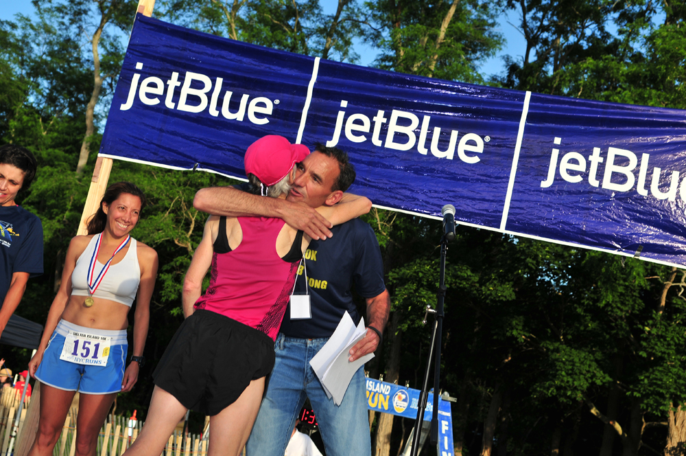 Joan Benoit Samuelson and race announcer Dr. Frank Adipietro share an embrace following the race. (Credit: Bill Landon)