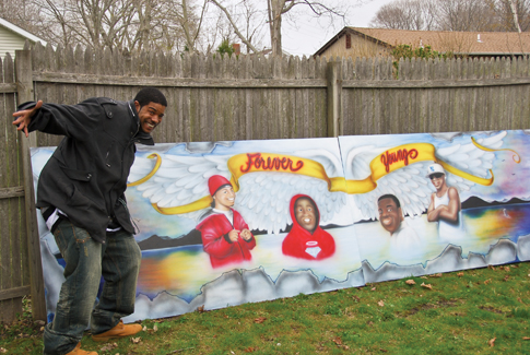 John R. Mims Jr. with the mural he created for Saturday's Global Youth Services Day cleanup at the Third Street basketball courts in Greenport. The mural honors four Greenport youths, Michael Brown, Corey Freeman, Kyle Rose and Naquawn Treadwell, who died in accidents in recent years. Members of Youth Engaged in Service also spruced up the park and painted and planted flower boxes.